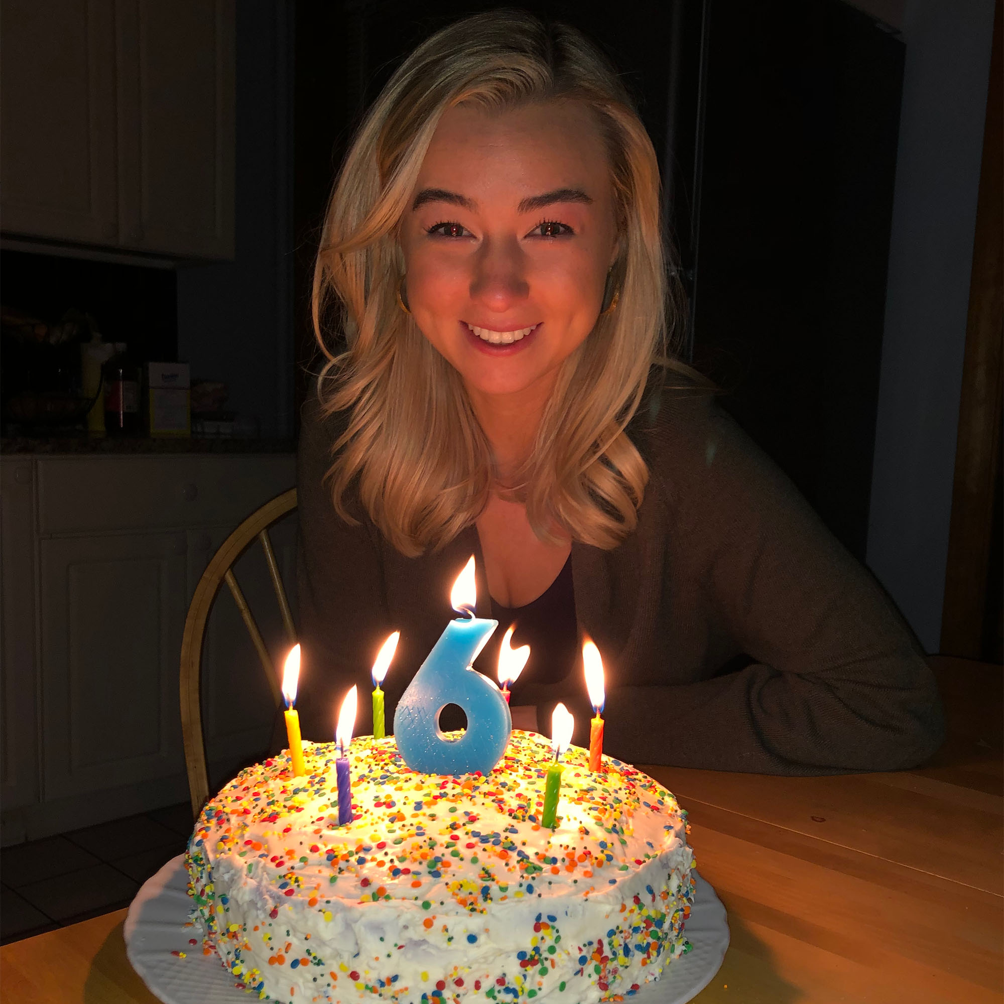 Photo: A young blonde woman in front of a cake with a large #6 candle on it