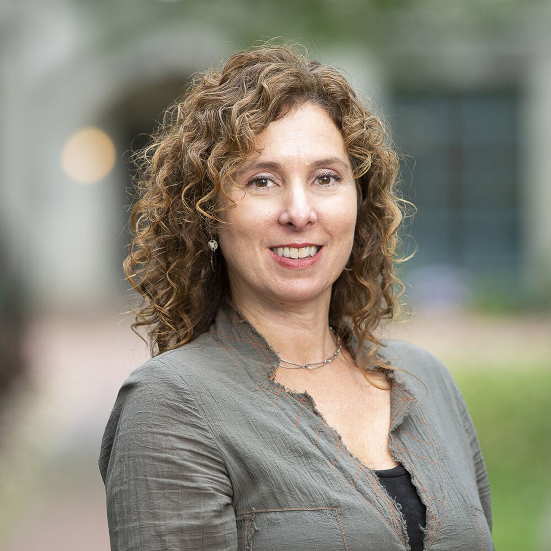 Photo: A white woman with light brown curly hair, Bronwyn Keefe, poses for a photo with a gray blazer. She smiles for the photo.