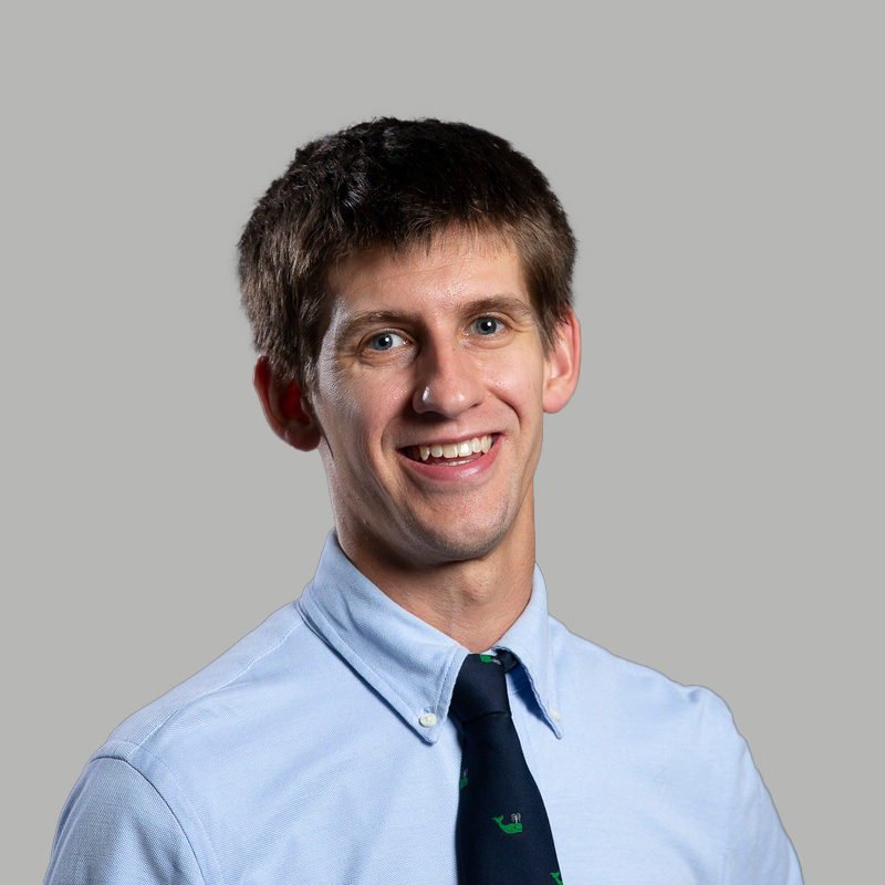 Photo: A young white man wearing a collared shirt and tie poses for a formal portrait headshot