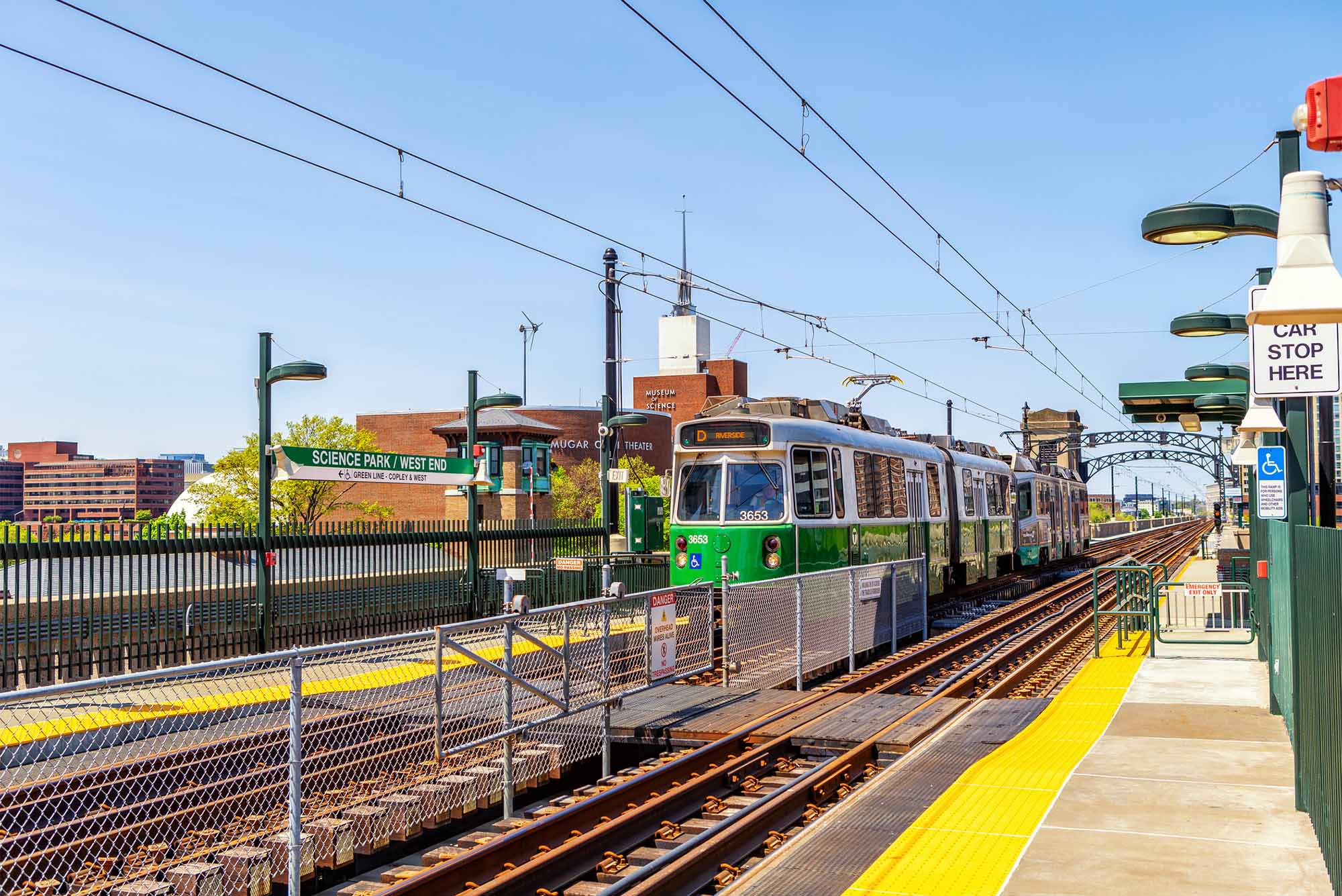 Photo: An MBTA green line train sitting at a station outside in Boston on a sunny day