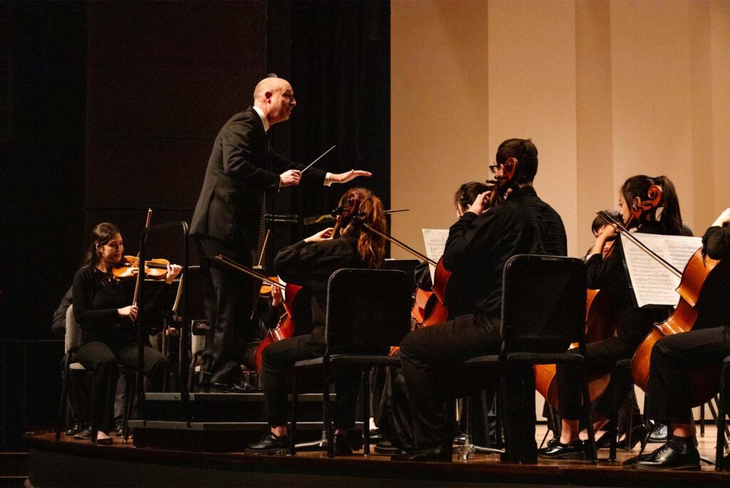 Photo: An orchestra conductor in front of a large group of stringed instrument musicians