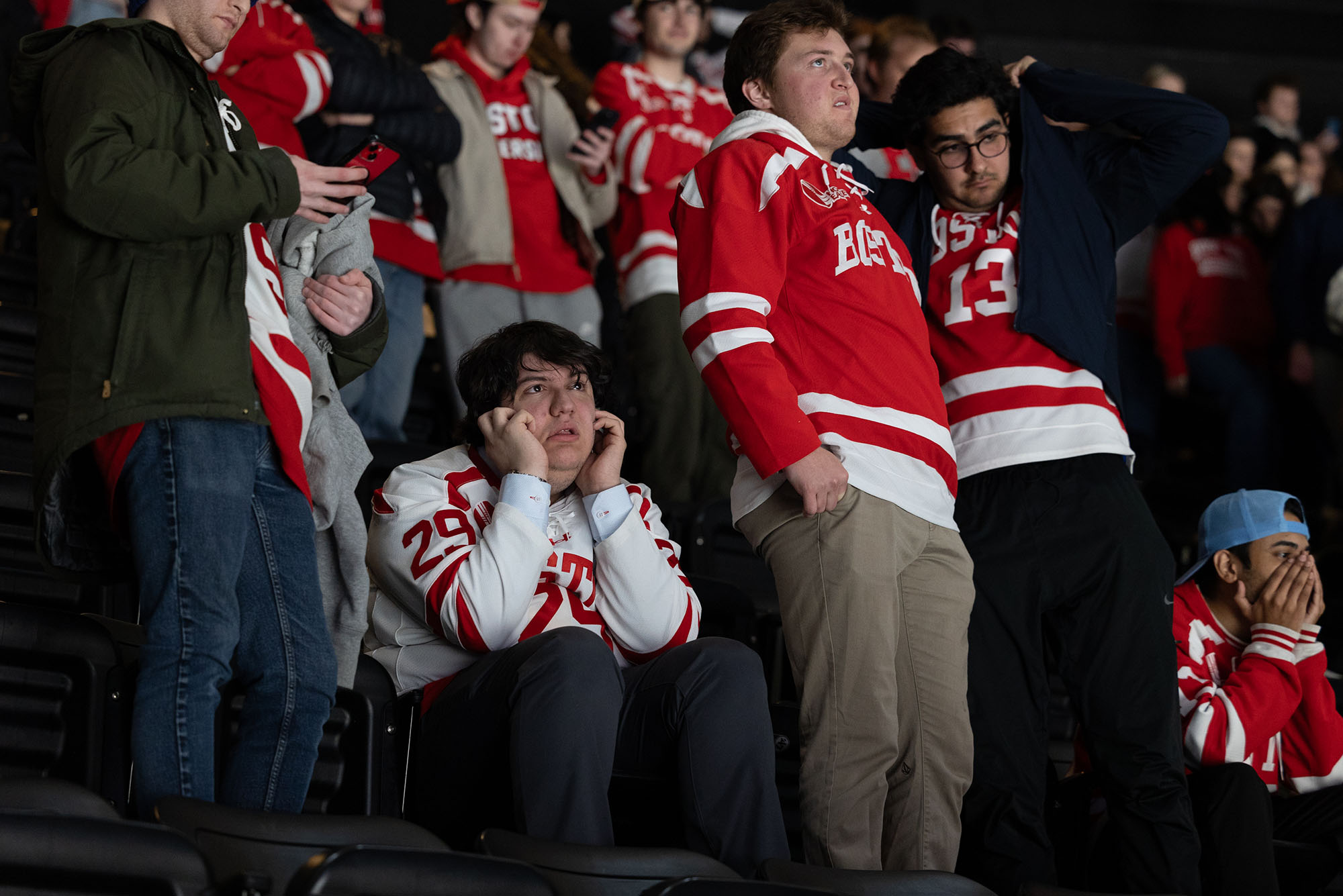 Photo: A crowd of fans for BU men's hockey hold their heads as BU team loses their lead. They wear various types of jerseys and merch.