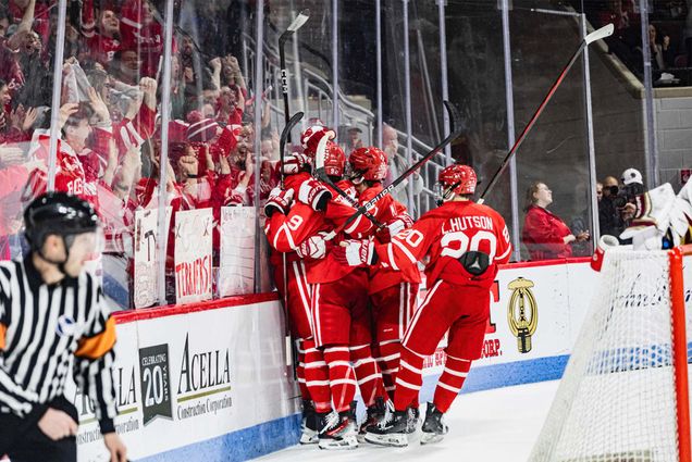 Photo: A large group of college hockey players celebrate near their bench in red jerseys as an onlooking crowd goes wild