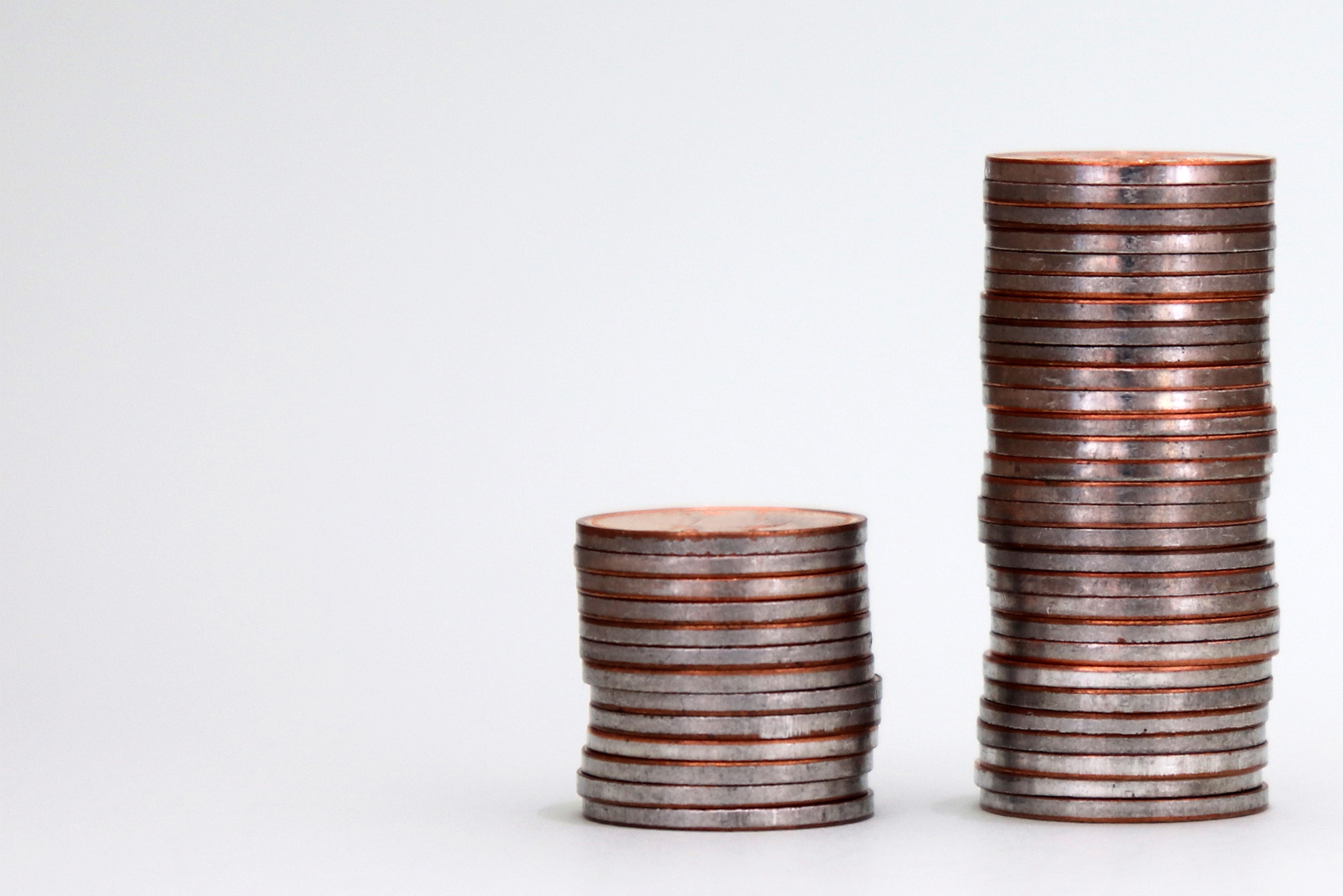 Photo: Two stacks of coins, one large and one small. Depicts wealth inequality