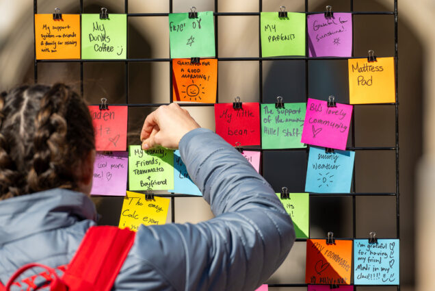 Photo: A college student with braids sticks a post-it note to a board filled with other notes