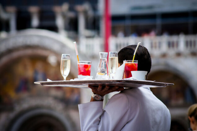 Photo: A stock image of a waiter delivering drinks in a white coat and slick back hair.