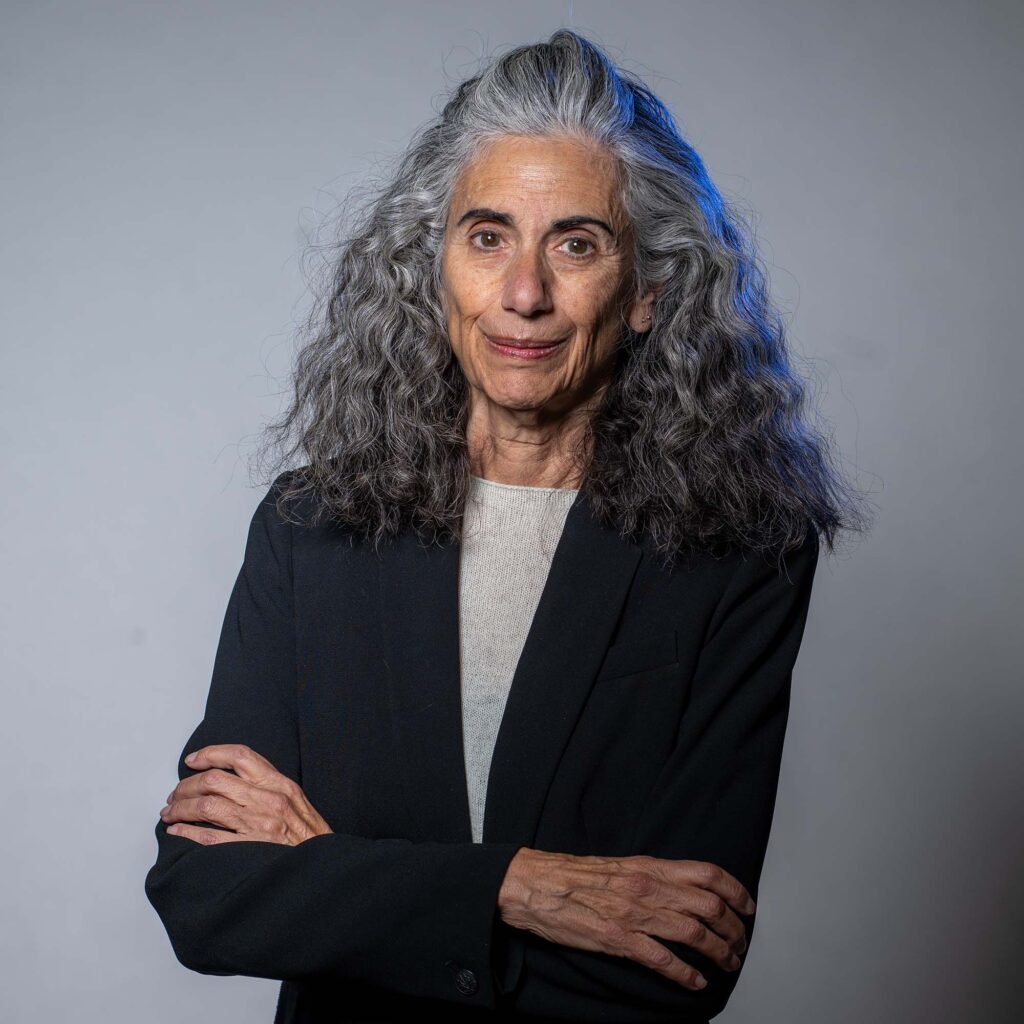 Photo: A woman with long curly hair wearing a dark suit jacket crosses her arms in this formal portrait 