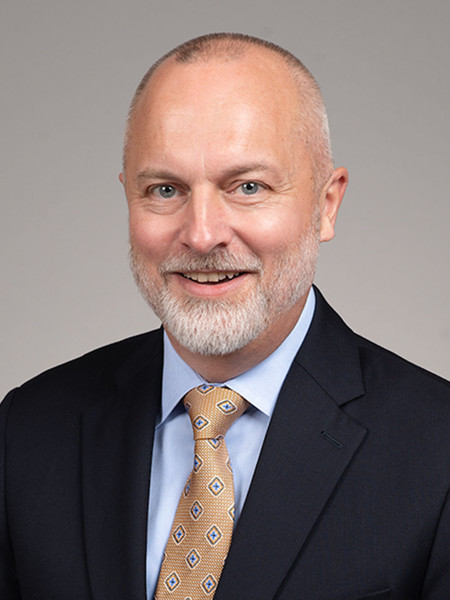 Photo: A white man wearing a suit and golden tie with a soft smile