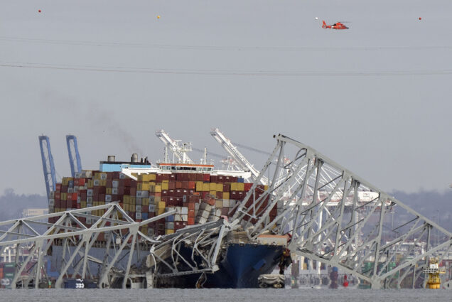 Photo: A helicopter flies over a container ship as it rests against wreckage of the Francis Scott Key Bridge after the container ship ran into the bridge, causing the collapse.