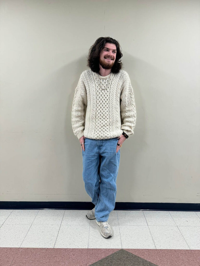 Photo: Jackson Cross, a young man wearing gray New Balances, baggy light blue jeans, and a knitted cream sweater.