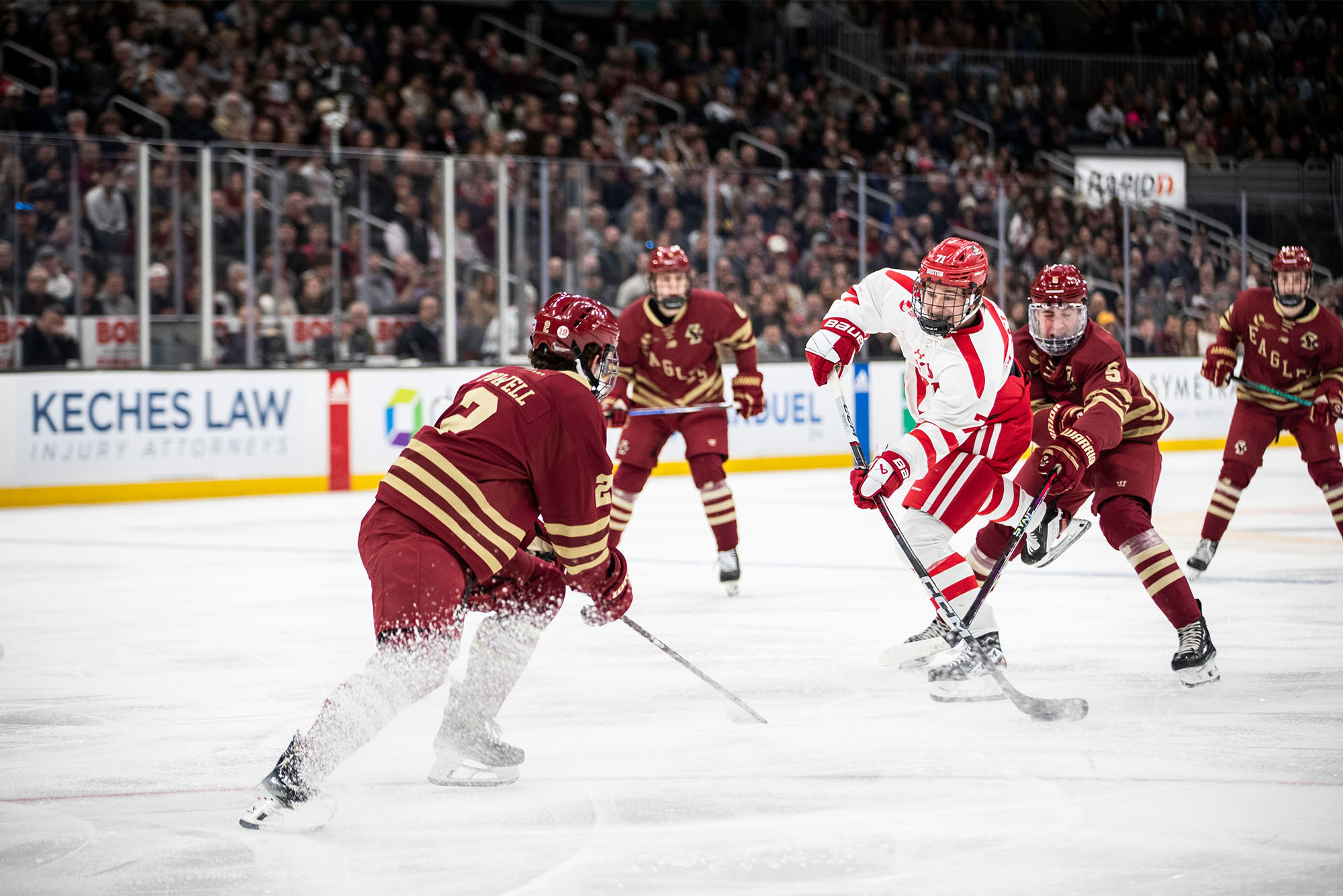 Photo: A BU college hockey player in a red and white jersey skates past players in dark maroon jerseys to fire a shot on net