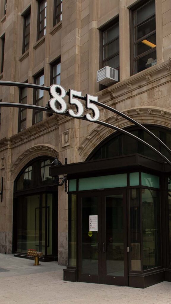 Photo: A large building with tan-colored stone and black doors. There is a black metal arch with the numbers "855" outside of it