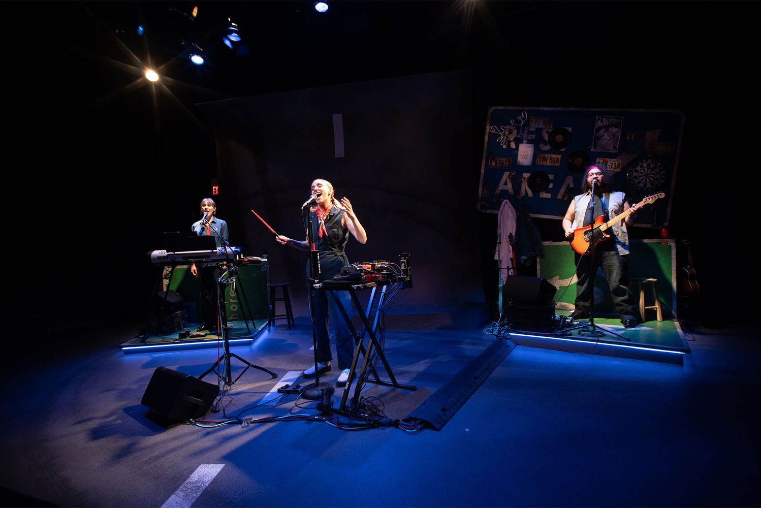 Photo: A performer stands in the middle of a stage lit with blue spot lights, a keyboardist and bassist flank the singer in the center