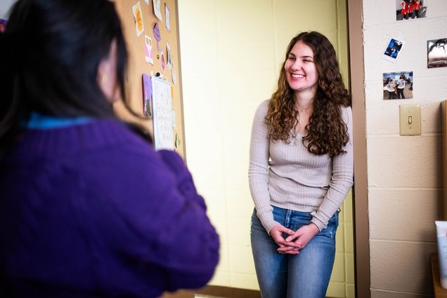 Photo: Danielle Vella, a white woman with long curly hair wearing a taupe long sleeve top, the RA at Sleeper Hall talks with a student