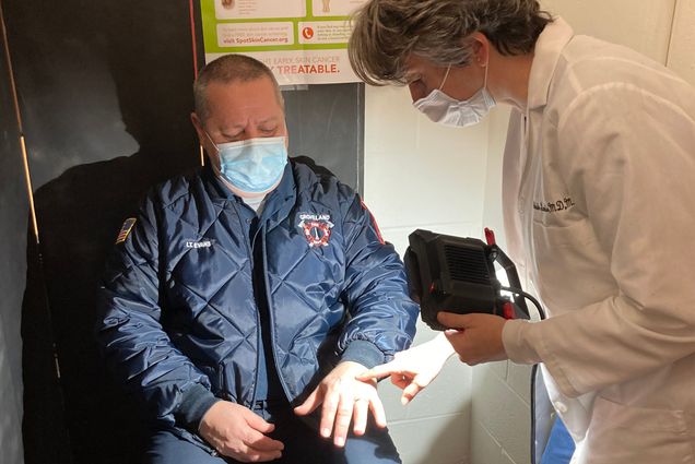 Photo: A doctor examines an older man's hands under a bright flashlight