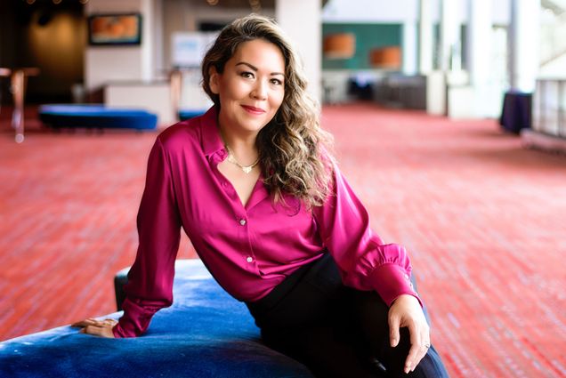 Photo: A woman in an elegant shirt with long dark hair sitting on a blue couch