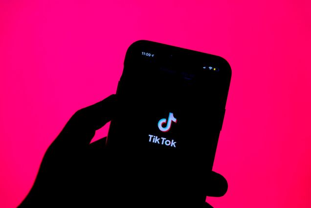 Photo: A stock image of a person holding a iPhone with a TikTok image on it and a bright pink background.