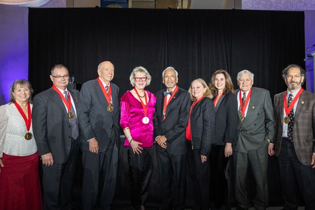 Photo: A group of 9 people in suits and elegant formal attire pose for a portrait