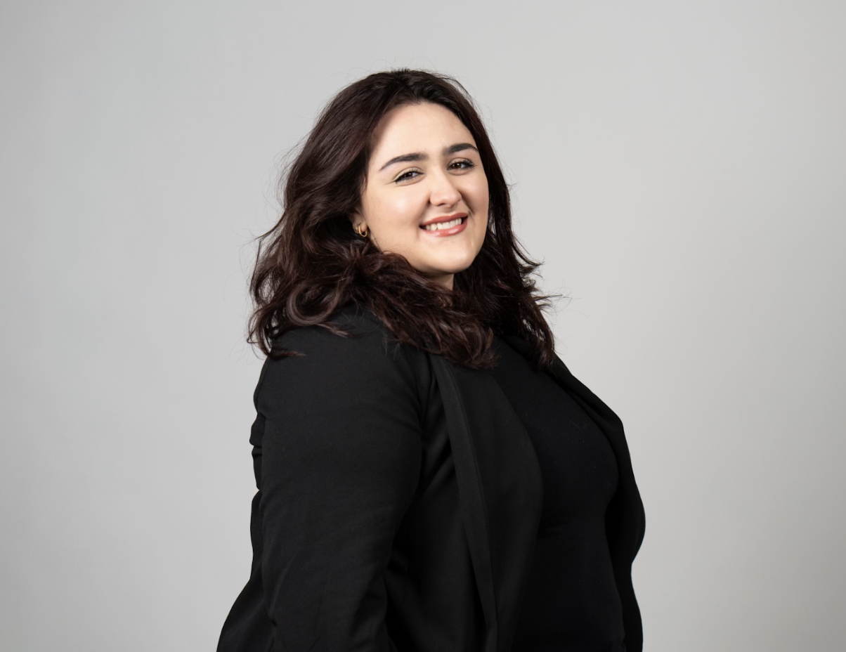 Boston University student Melaina (Lainey) Roberto (COM’24). She is wearing a black longsleeve top in front of a grey, professional background. She is smiling at the camera.