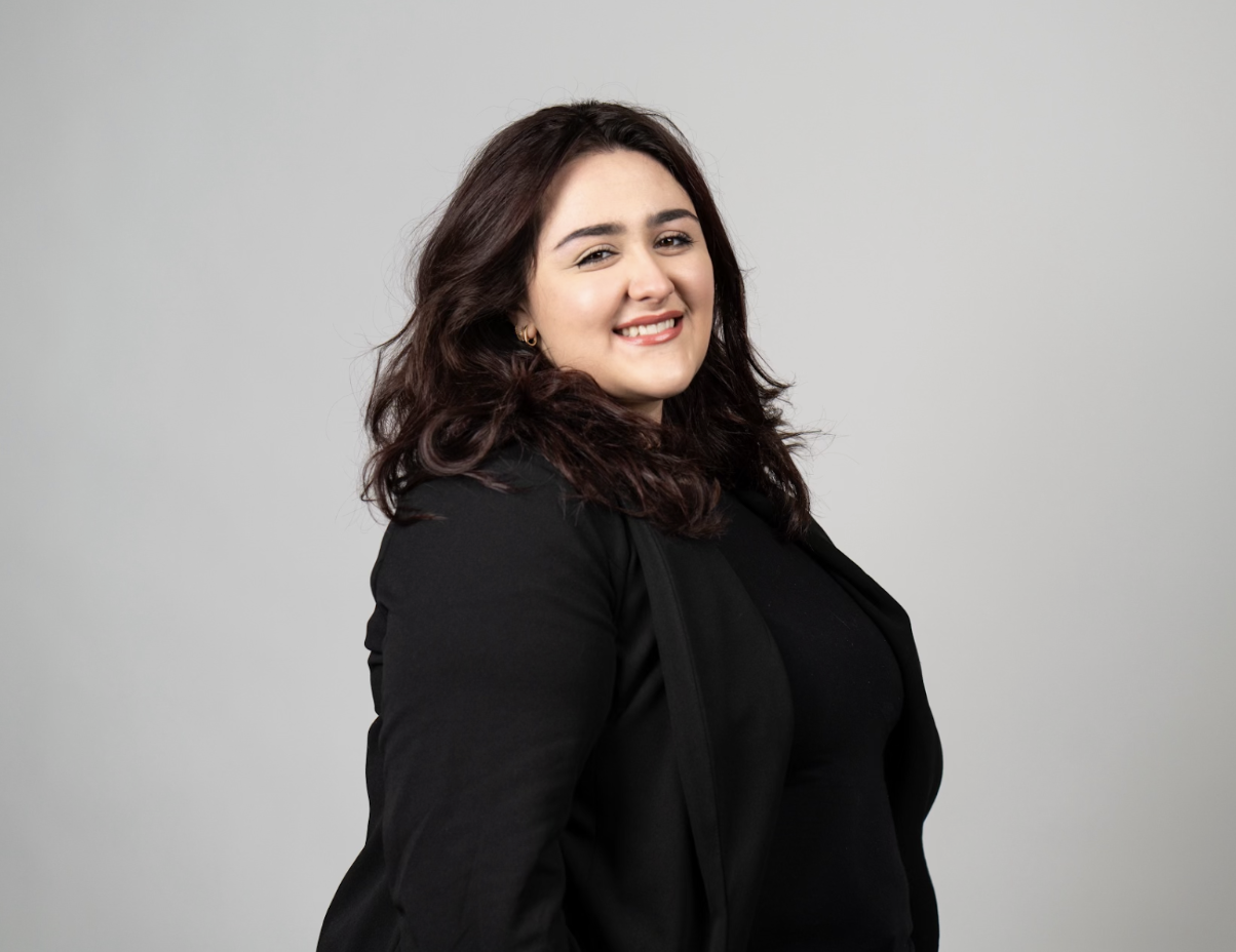 Boston University student  Melaina (Lainey) Roberto (COM’24). She is wearing a black longsleeve top in front of a grey, professional background. She is smiling at the camera. 