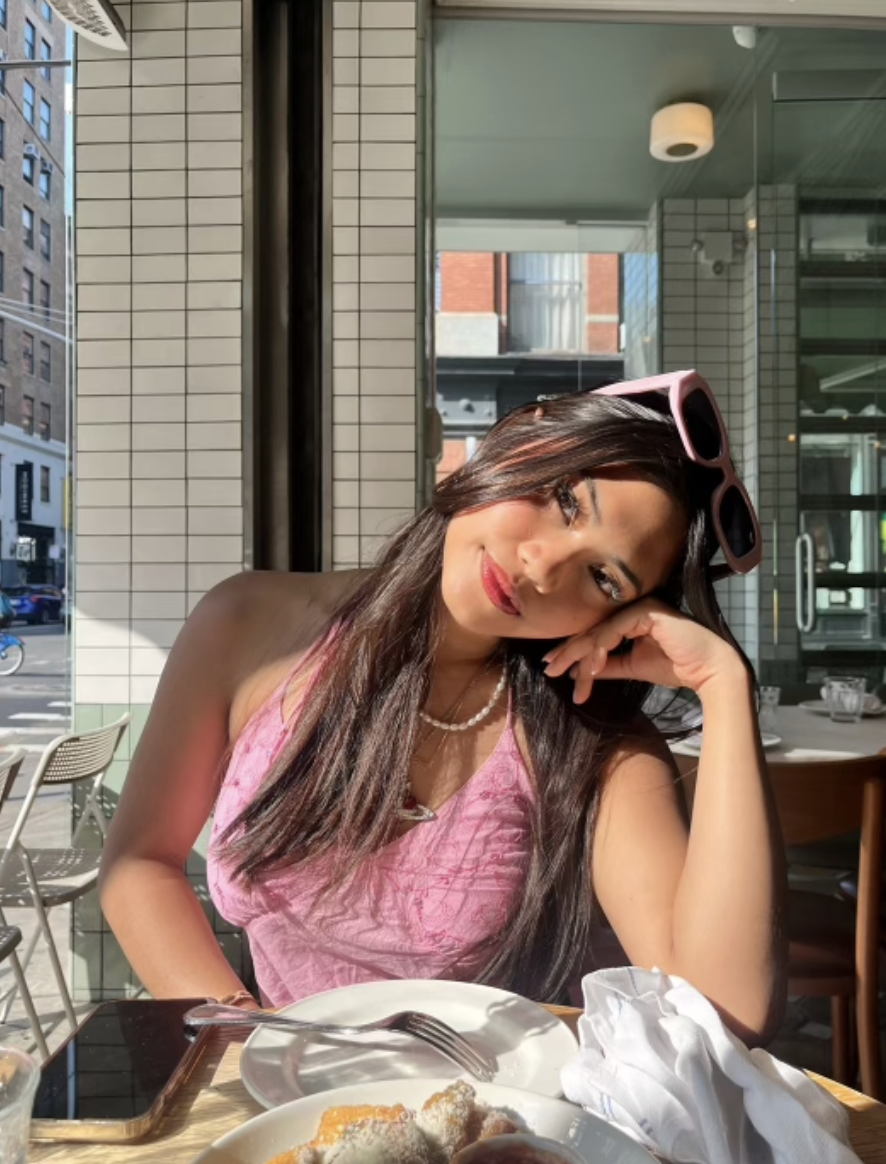 Boston University student Sisi Amara (Questrom ’24). She is at a restaurant with her head leaning on her hand. She has on a pink top with white sunglasses on her head.