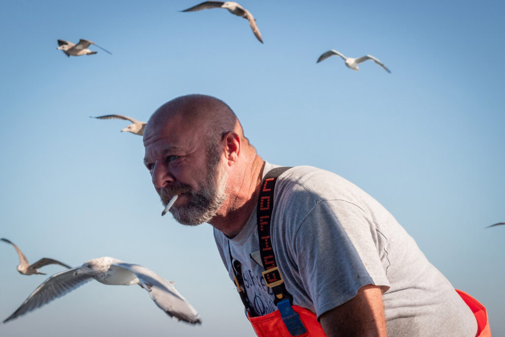 Photo: A fisherman leans on his hands as he takes a smoke break, a handful a seagulls flying around him artistically.