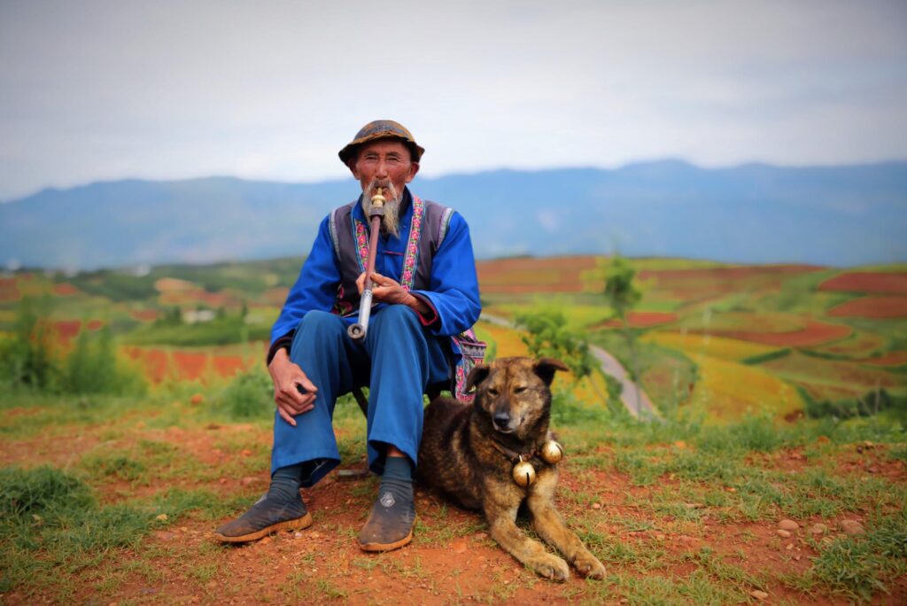 Photo: A man in China, Yunnan sitting playing his flute dressed in traditional farming garb. His dog sits next to him, content.