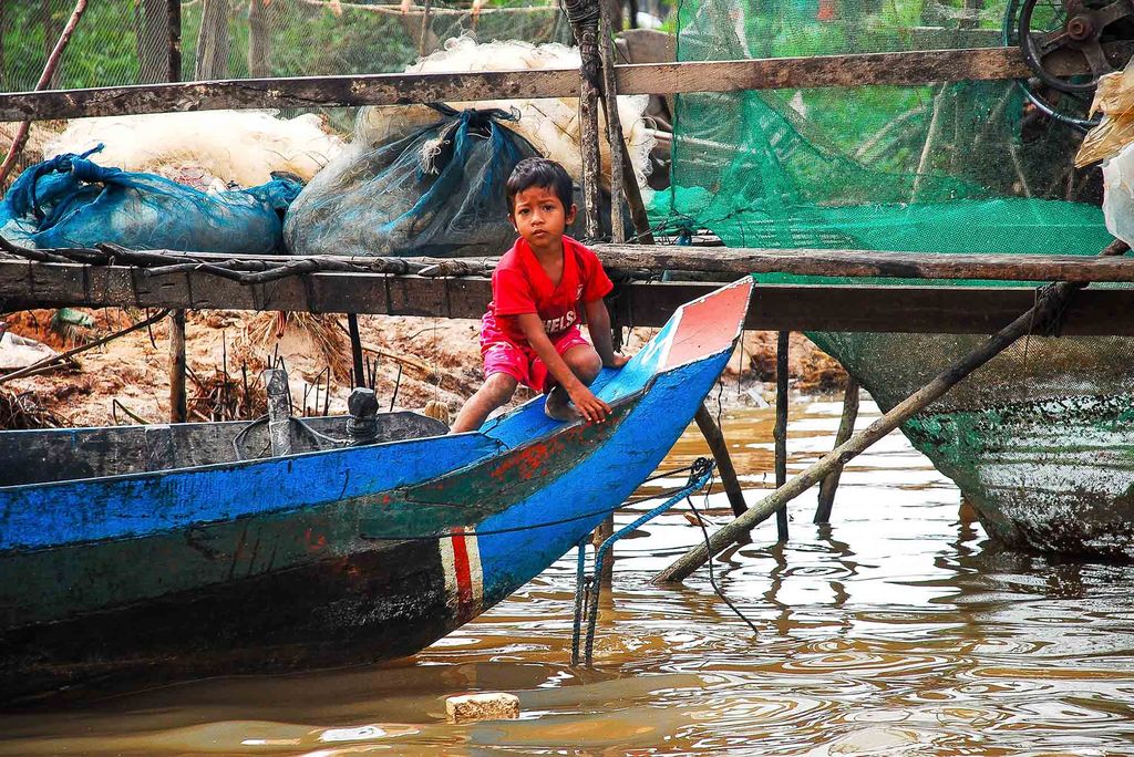 Photo: A shot of a boy on a blue canoe, sitting on the edge while the canoe sits at the edge of the water.