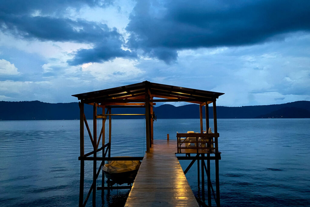 Photo: A shot of a dock at dusk, with the clouds in the sky and a faint light on the wooden pathway up to the dock.