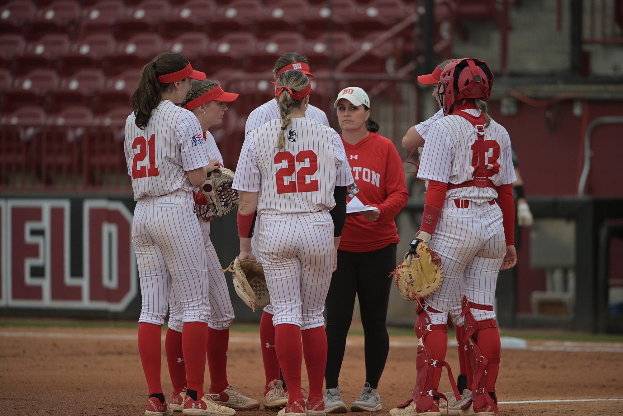Photo: Ashley Waters, a short white woman with her team. They surround her as she gives advice close to the dugout.