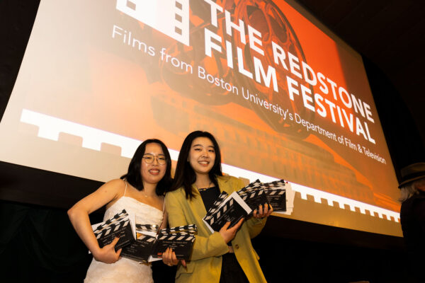 Photo: A picture of two girls in front of a projector screen holding up movie awards shaped like clapperboards