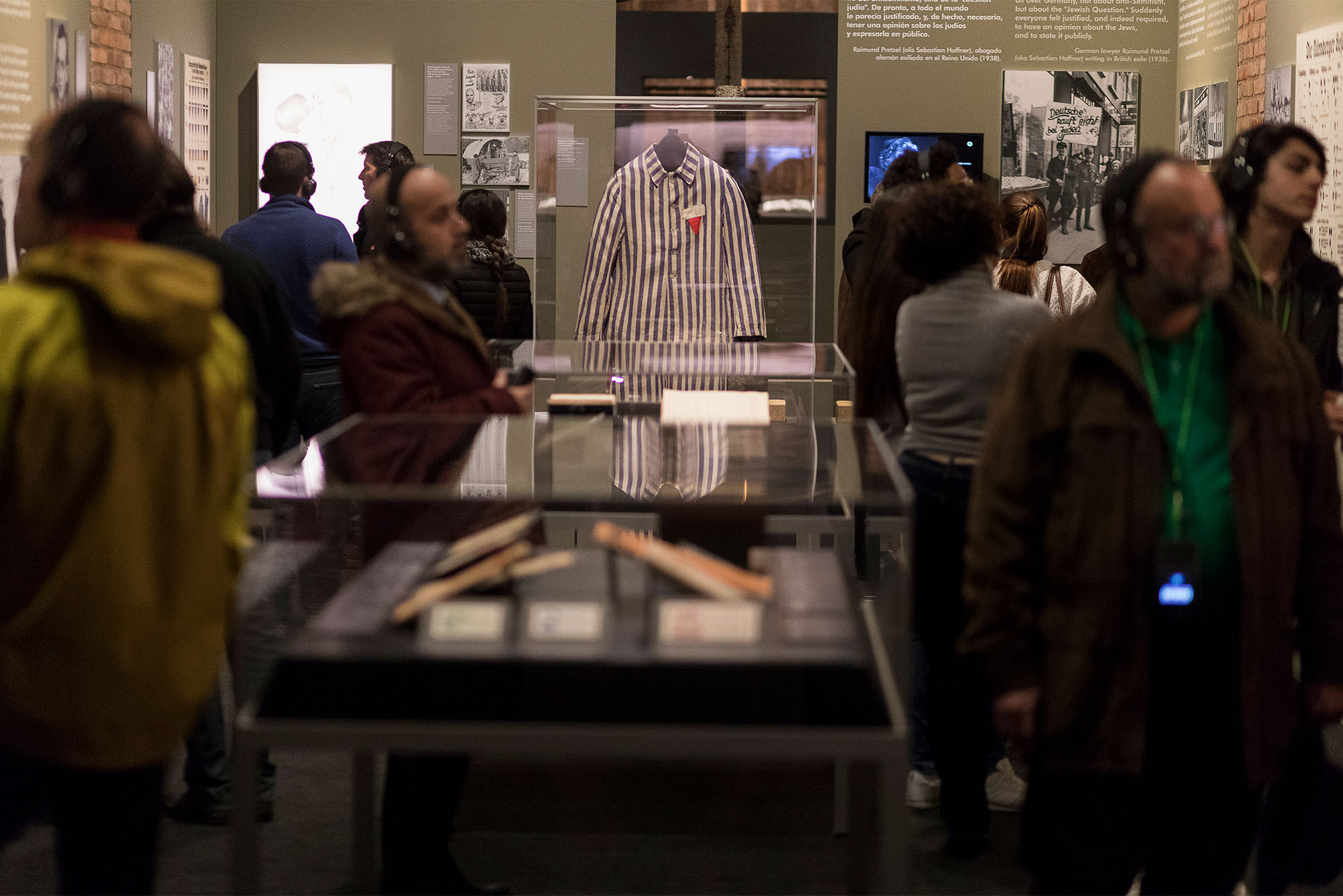Photo: groups of people gathering around a museum case filled with objects taken from those imprisoned at Auschwitz in Nazi Germany