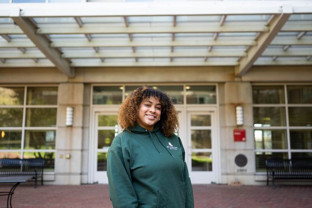 Photo: Yadira Cabrera, a young woman with shoulder length curly hair and bangs, at StuVi dorm buildings front door.