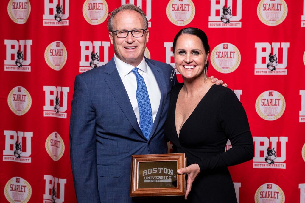 Photo: A picture of a man in a blue suit and a woman in a black dress posing with a Boston University plaque. There is a red background that says "BU" behind them