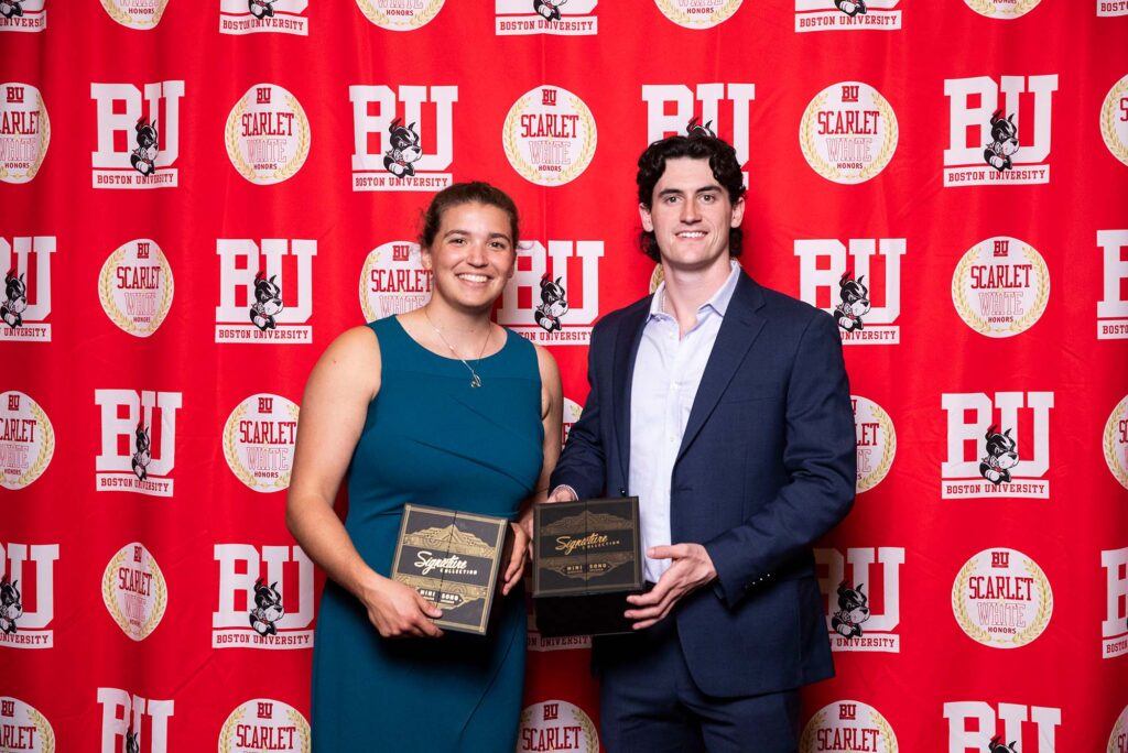 Photo: A picture of a man and a woman holding Boston University awards. There is a red background that says "BU" behind them