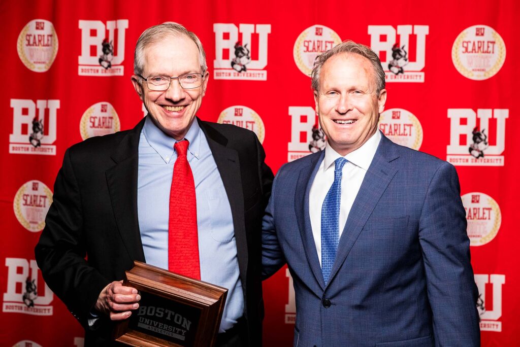 Photo: A picture of two men in suits posing with an award. They are standing in front of a red background that says "BU"