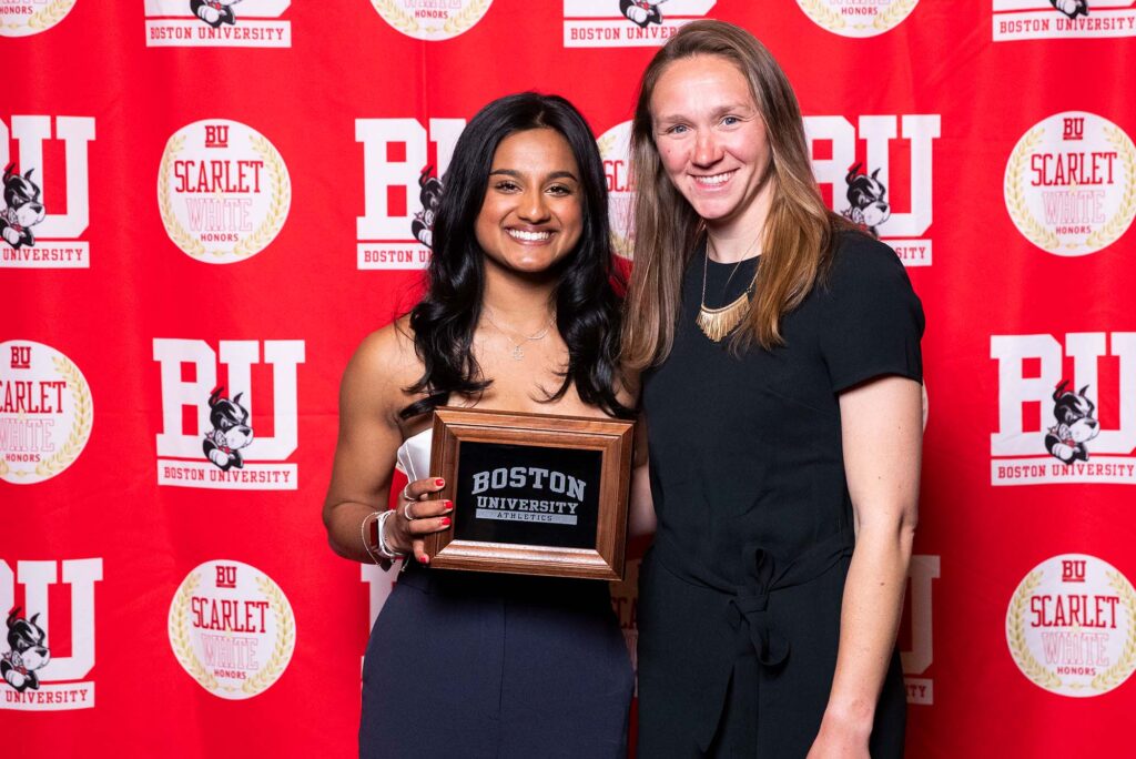Photo: Two women in black dresses posing with a plaque. They are standing in front of a red background that says "BU"