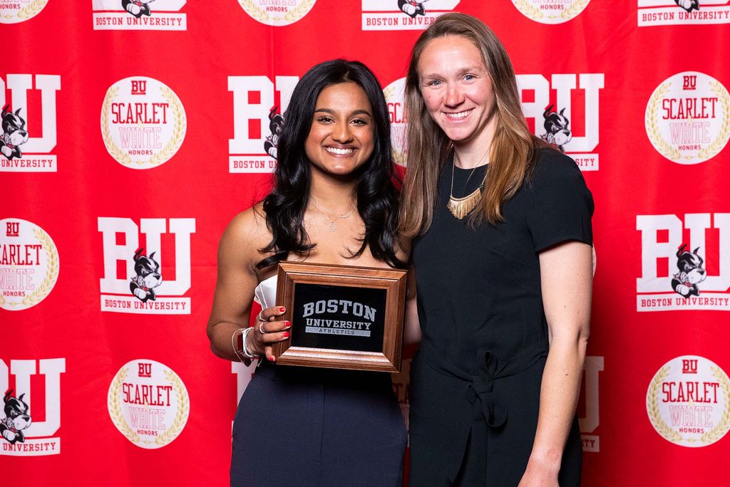 Photo: Two women in black dresses posing with a plaque. They are standing in front of a red background that says "BU"