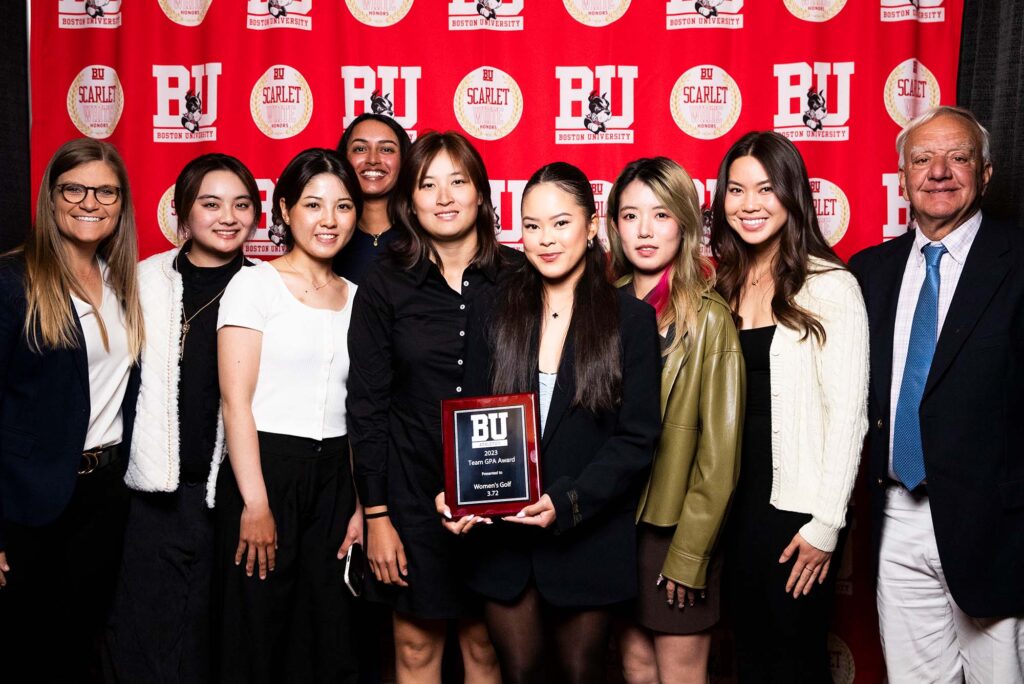 Photo: A picture of a large group holding up a Boston University award. There is a red background that says "BU" behind them