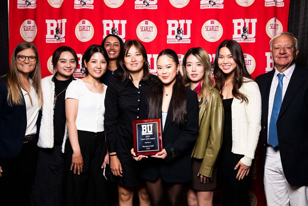 Photo: A picture of a large group holding up a Boston University award. There is a red background that says "BU" behind them