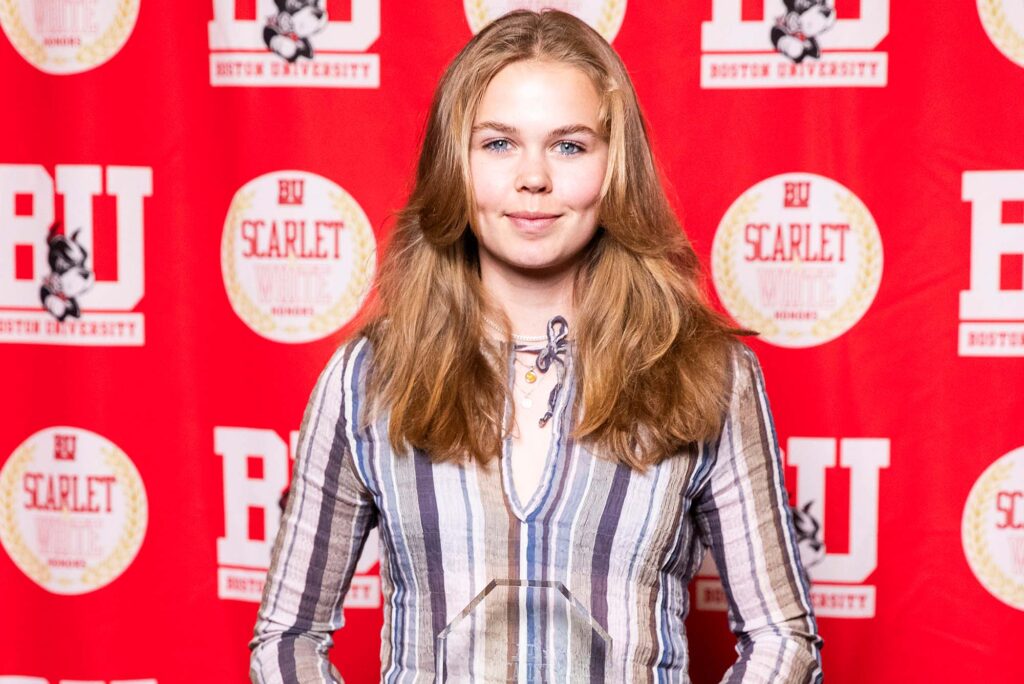Photo: A woman with light hair in a patterned long-sleeve shirt holding a clear award. She is standing in front of a red background that says "BU"