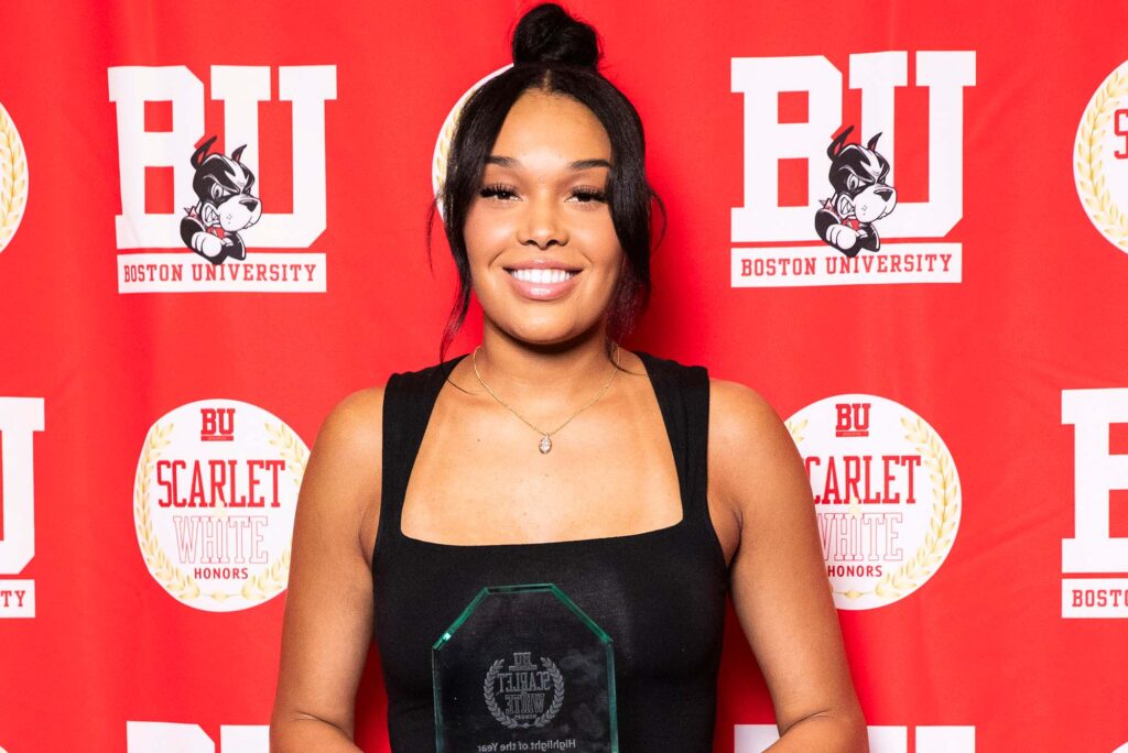 Photo: A picture of a woman in a black dress posing with a clear Boston University award. She is smiling and posing in front of a red background that says "BU"