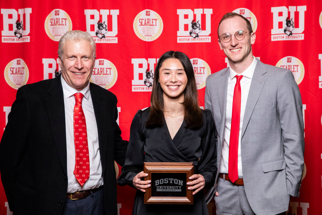 Photo: A picture of people posing in front of a red background that says "BU." There are three people with a woman in the middle holding an award and men in suits on either side