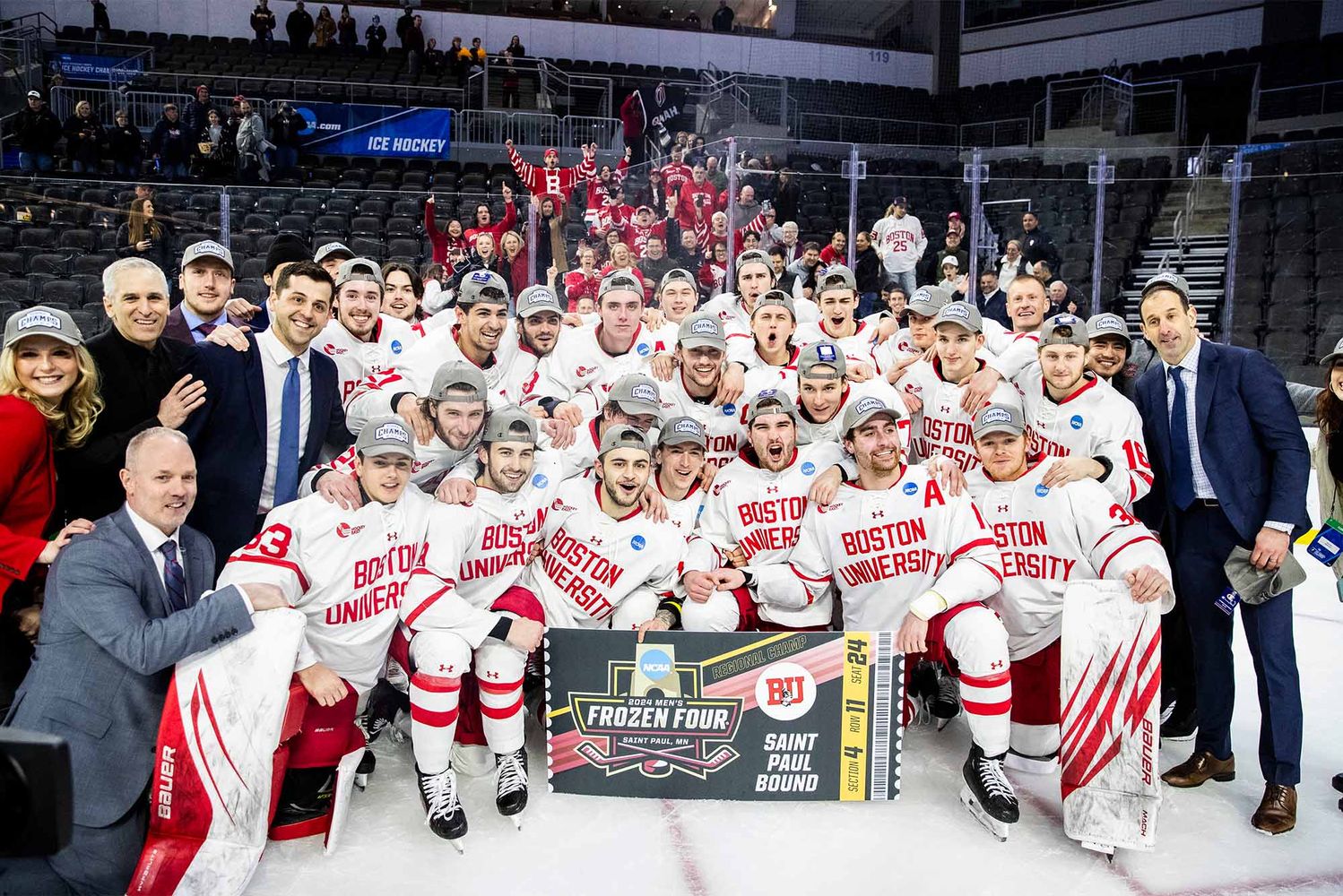 Photo: The Boston University men’s ice hockey team after defeating Minnesota in the NCAA Sioux Falls Regional final. A large group of men are wearing red hockey jerseys and celebrating while holding up a trophy