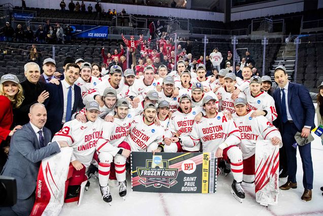Photo: The Boston University men’s ice hockey team after defeating Minnesota in the NCAA Sioux Falls Regional final. A large group of men are wearing red hockey jerseys and celebrating while holding up a trophy
