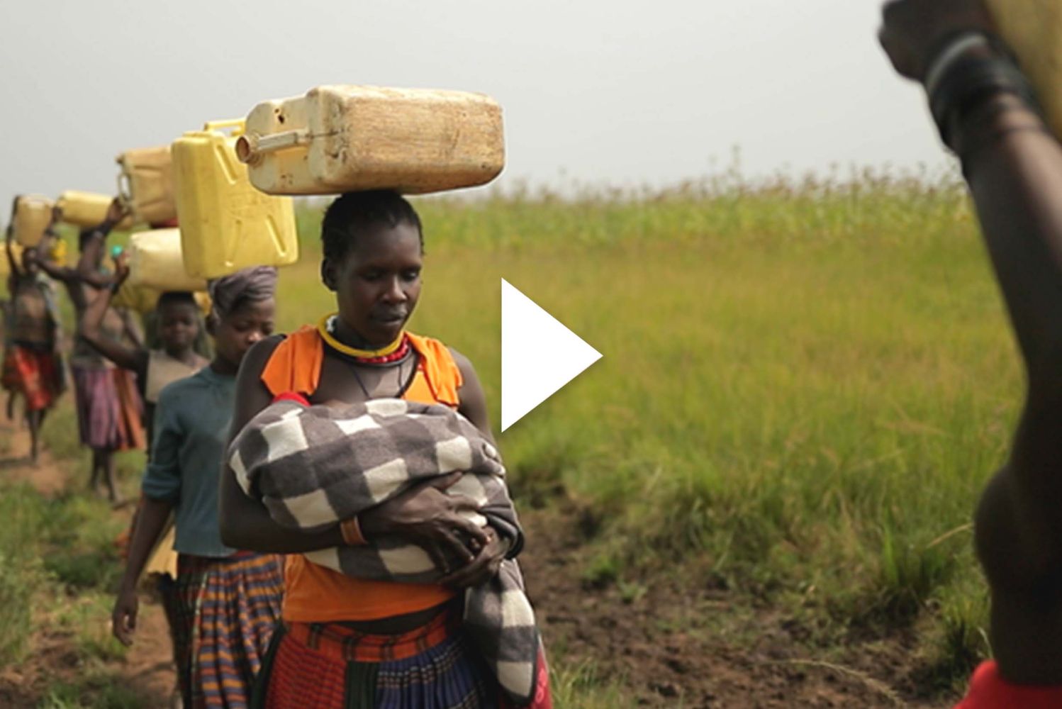 Photo: A picture of women walking and carrying things on their heads. There is a play button overlay