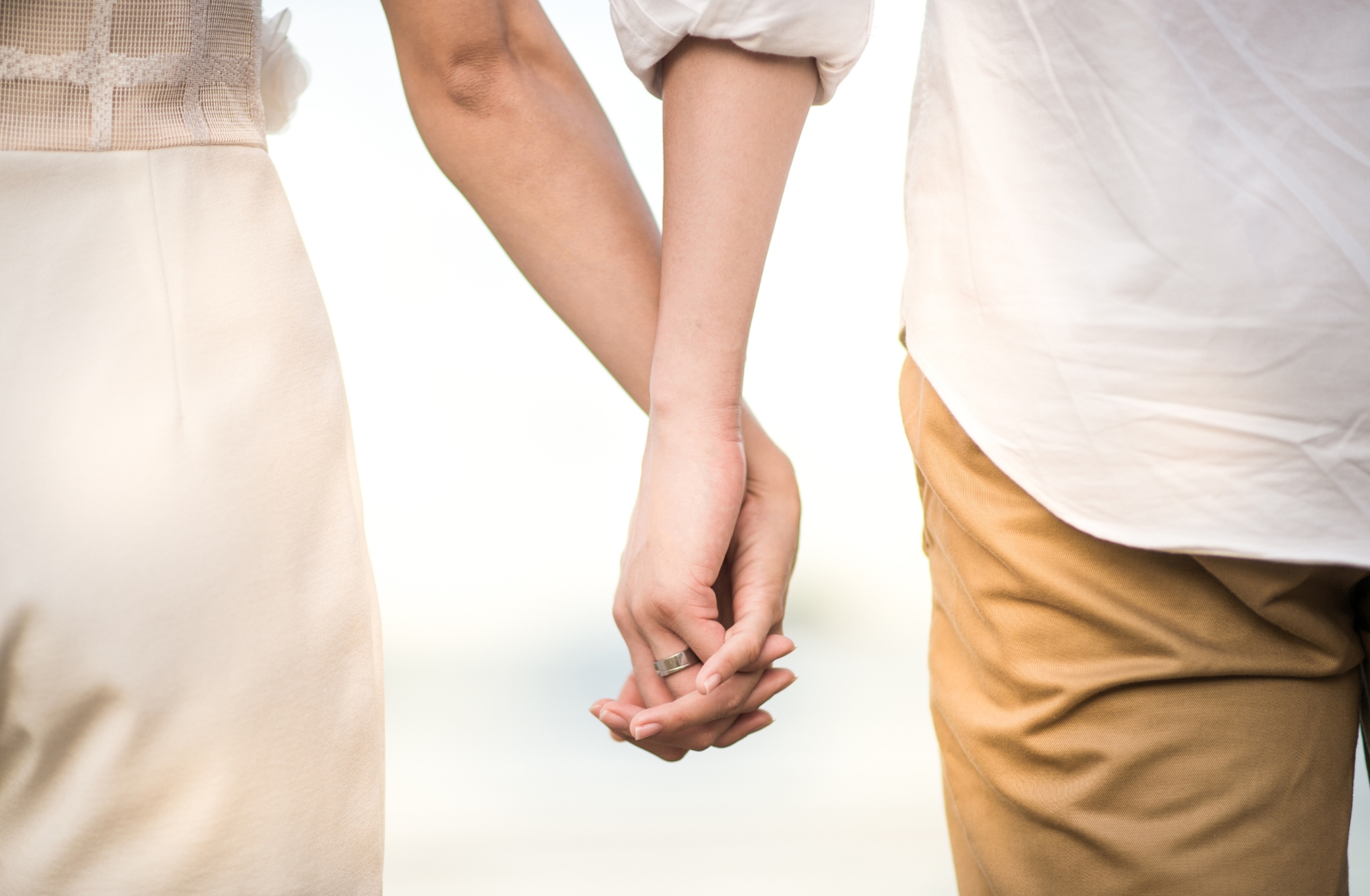 Man and woman holding hands. The woman is wearing a white dress while the man is wearing a white shirt and tan pants.