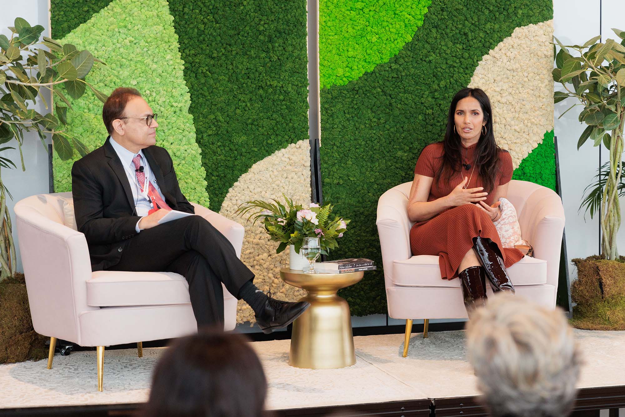 Photo: A picture of two people sitting in separate armchairs. There is a small table between them with flowers and books on it. They are dressed in formal attire