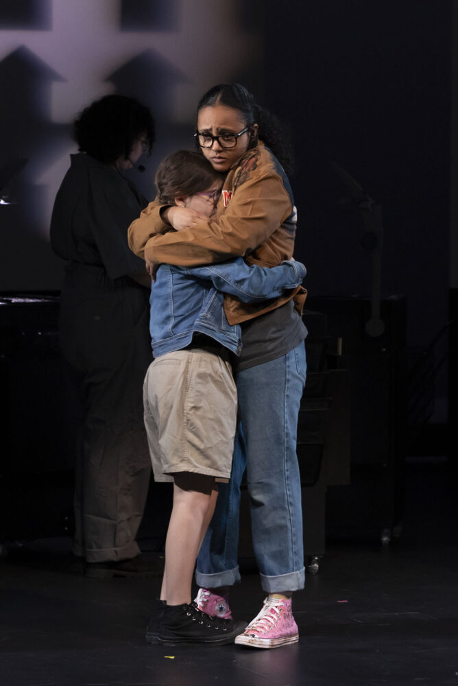 Photo: Two people hugging on stage. Eviva Rose (left) and Beza Mekonnen during a dress rehearsal for the Wheelock Family Theatre’s of A Wrinkle in Time.