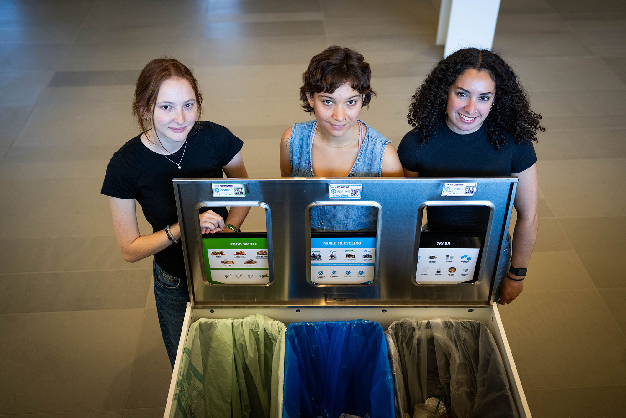 Photo: (Left to right) Tess Shotland, a woman with auburn hair and a black tshirt Cece Lagomarsino, a woman with short hair and a jean overall, and Nina Palmeon, a woman with long curly hair and a black tshirt posing with the waste disposal system at CDS.